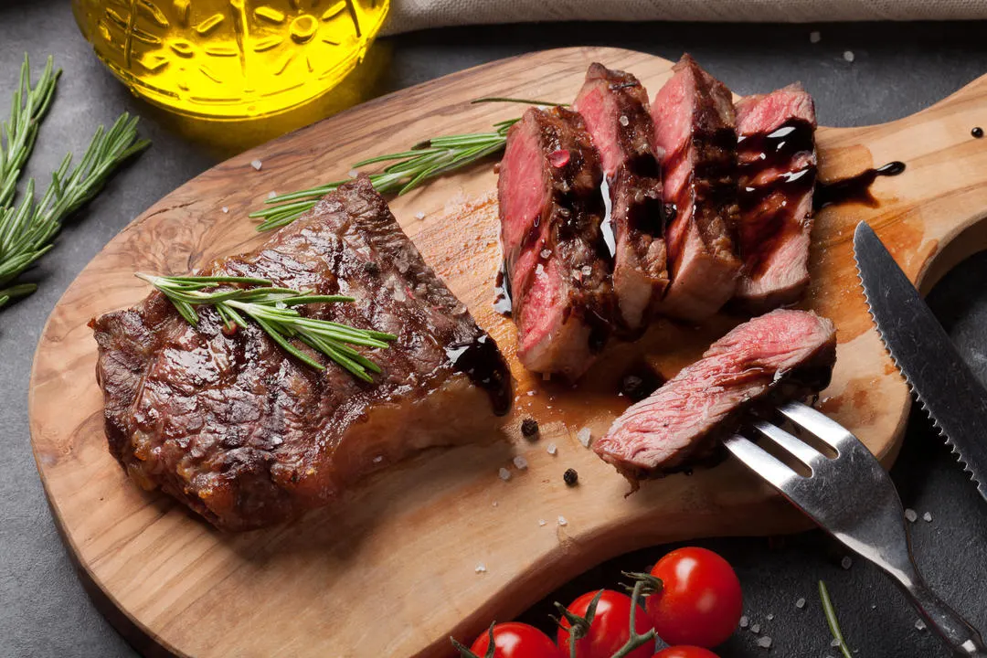 Pièce de viande sur planche en bois avec romarin, tomates cerises et huile d'olive