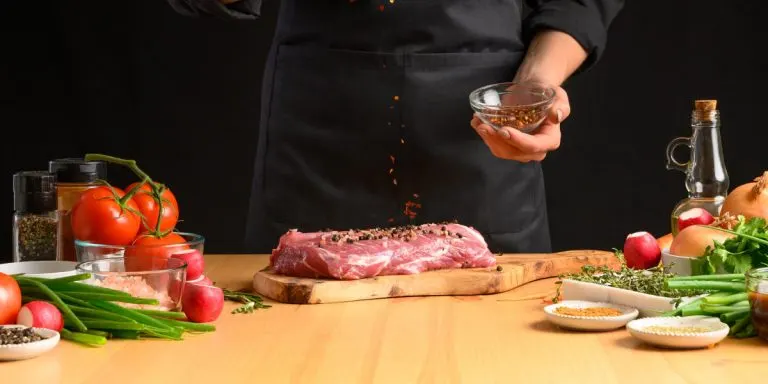 Illustration La Gastronomie : boucher saupoudrant des épices sur une pièce de viande entourée de légumes