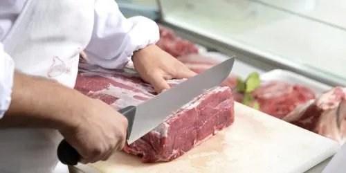 Boucher en blouse blanche découpant une pièce de viande au comptoir