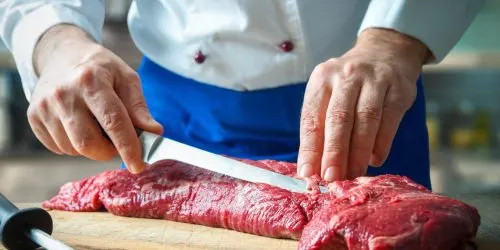 Boucher parant une pièce de bœuf au couteau sur une planche en bois