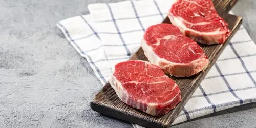 Trois pavés de bœuf crus présentés sur une planche à découper en bois